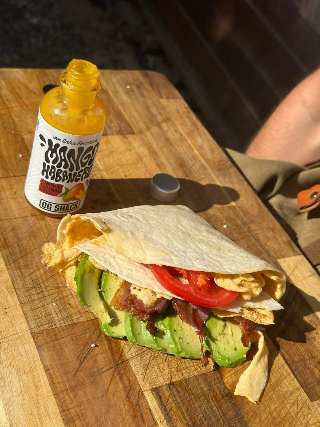 Wrap abierto con huevo, tomate y aguacate sobre una tabla junto a una botella de salsa Mango Habanero de OG Shack.